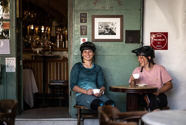 Zwei Frauen mit Fahrradhelm trinken einen Kaffee